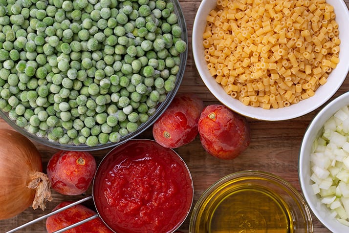 Ingredients for pasta piselli. Olive oil, onion, tomatoes, and green peas.